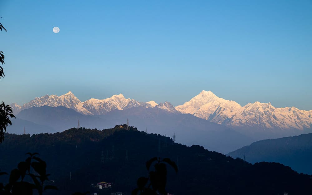The Kangchenjunga massif at moonrise above the forested hills
